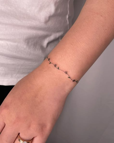 60+ Best Daisy Tattoo Ideas & All You Must Know About Them - InkMatch Dainty Flower Chain Tattoo, Daisy Ring Tattoo, Daisy Chain Anklet Tattoo, Daisy Chain Tattoo Wrist, Constellation Wrap Around Tattoo, Cute Bracelet Tattoos, Delicate Daisy Tattoo Simple, Fine Line Daisy Chain Tattoo, Daisy Chain Bracelet Tattoo