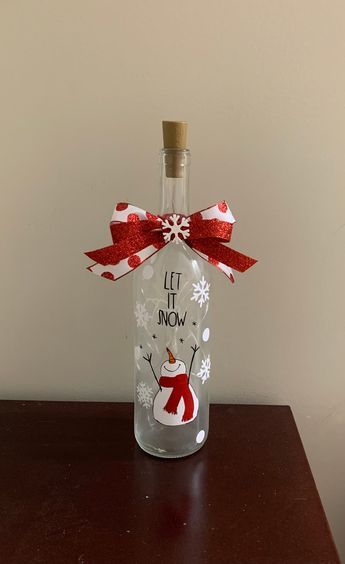 Get festive by adding a wine bottle light to your Christmas decor! LED battery operated Christmas wine bottle lights.   "Let it Snow " Snowman design. Extra batteries included These make great gifts!  Made out of clear wine bottle, with vinyl and frosted finish. Decorated with ribbon. If ordering multiple items, please send me a message and I will create a custom listing for you to bundle and save on shipping. Wine Bottle Christmas Craft, Light Up Wine Bottles Diy Christmas, Holiday Painted Wine Bottles, Diy Painted Bottles Ideas, Christmas Crafts With Wine Bottles, Christmas Decorated Bottles, Christmas Glass Bottle Crafts, Gingerbread Wine Bottle, Bottle Art For Christmas