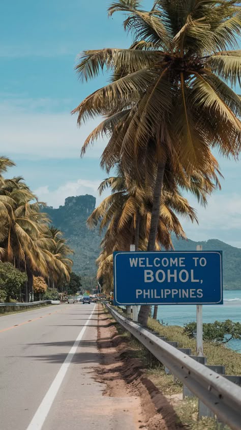 Welcome to Bohol, Philippines" sign by a palm-lined road, with mountains, the sea, and a clear sky in the background. Places To Travel In Philippines, Traveling To The Philippines, Travel Philippines Aesthetic, Bohol Chocolate Hills Philippines, Philippines Vision Board, Bohol Philippines Aesthetic, Nature In Philippines, Phillipines Travel Aesthetic, Phillipines Aesthetic