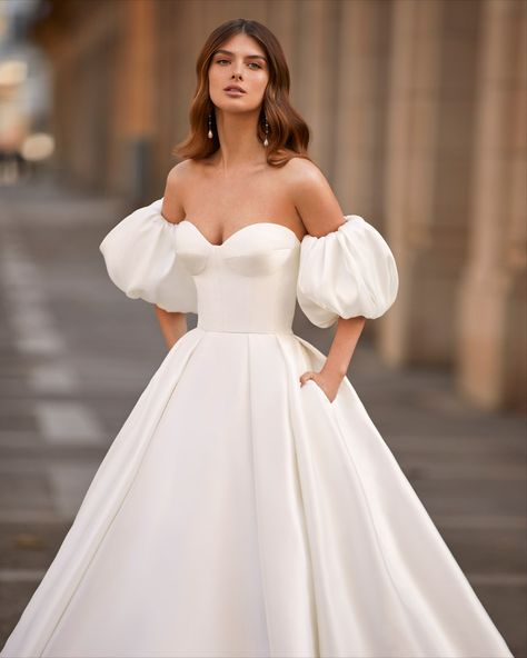 Luna Novias | This minimalist wedding dress features a tailored bodice with a voluminous pleated princess skirt and removable puffed sleeves. Princess Style Wedding Dresses, Embroidered Wedding Gown, Beaded Wedding Gowns, Classy Prom Dresses, Minimalist Wedding Dresses, Princess Skirt, Fashion Gowns, Princess Wedding Dress, Strapless Neckline