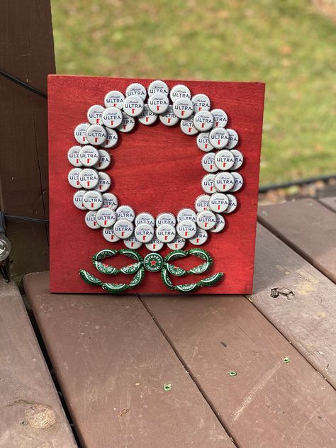 "This beautiful stained red poplar with a unique bottle cap design will really help change up your Christmas decor! Michelob Ultras are used for the white wreath and Heineken finishes the piece with a green bow. This is a great piece for any space during the holidays and the colors really catch the eye!  This piece is 11 1/2 \" x 11 1/2\" and about 1 1/2\" deep." Beer Cap Projects, Bottle Cap Design, Beer Bottle Cap Art, Bottle Top Art, Beer Bottle Cap Crafts, Plastic Bottle Tops, Beer Cap Art, Bottle Top Crafts, Bottle Cap Projects