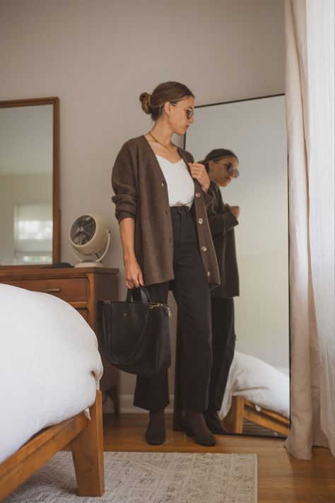 Ashley in her bedroom next to a bed and vintage dresser wearing a white silk cami, chocolate brown oversized cardigan, black cropped pants, brown sock booties, tortoiseshell sunglasses, and a black tote bag Brown Cardigan Work Outfit, Styling Brown Cardigan, Brown Button Up Cardigan Outfit, Black Cardigan Outfit Spring, How To Style A Brown Cardigan, Chocolate Brown Cardigan Outfit, Cardigan Button Up Outfit, Black Outfit Brown Boots, Outfits With Brown Cardigan