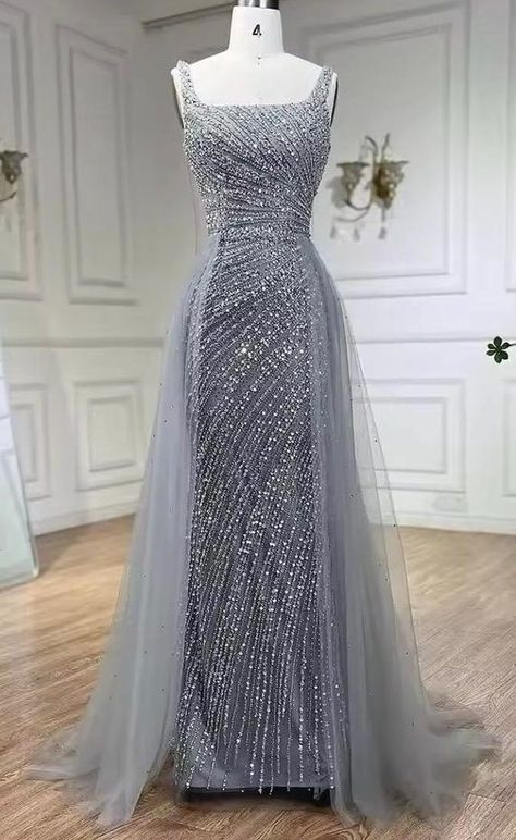 This  silver bead embellished gown with an overskirt is a show-stopping piece that exudes luxury and elegance. The gown is intricately adorned with shimmering silver beads, creating a dazzling effect that catches the light beautifully. The fitted silhouette of the gown enhances the natural curves, while the attached overskirt adds a dramatic and voluminous element, creating a sense of grandeur. This combination of the sleek, bead-embellished base and the flowing overskirt results in a balanced a Silver Gowns Elegant, Silver Dresses Elegant, Silver Dress Formal, Elegant Silver Dress, Farewell Dance, Overskirt Dress, Silver Ball Gown, Silver Wedding Gowns, Gown With Overskirt