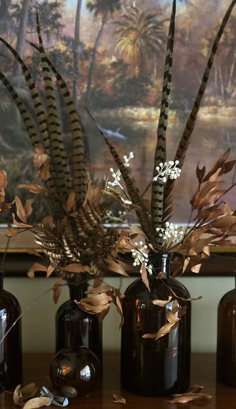 Amber glass and pheasant feathers Pheasant Feather Decor Wedding, Turkey Feather Centerpiece, Pheasant Wedding Decor, Pheasant Feather Centerpieces, Hunting Centerpieces, Feather Display Ideas, Curiosity Cupboard, Barn Bar Ideas, Fall Mantle Ideas