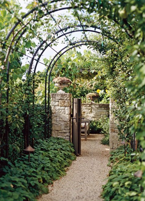 Arch trellises connected within a metal framework line up to create a tunnel that guides visitors from one area to the next. The striking construction frames a foliage-lined gravel walkway leading to a stone-walled outdoor room. #archtrellis #gardenarch #archwayideas #landscaping #bhg Metal Arbor, Garden Arch Trellis, Arch Trellis, Metal Pergola, Garden Vines, Garden Arches, Garden Arbor, Garden Entrance, Backyard Pergola