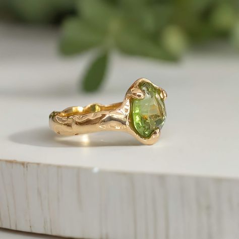 A beautifully handcrafted Peridot engagement ring, uniquely made with wax and cast in solid 14k gold. Its textured band lends a rustic charm to the elegant green stone, captured in a mesmerizing light play. This August birthstone ring is more than just jewelry—it's a poetic expression of individuality and lasting love, perfectly embodying your unique story. Available in sterling silver or solid 14k gold. Green Engagement Ring Silver Band, Light Green Ring, Weird Wedding Rings, Rings Engagement Unique, Ethereal Rings, Ethereal Engagement Ring, Peridot Ring Engagement, Organic Engagement Ring, August Jewelry