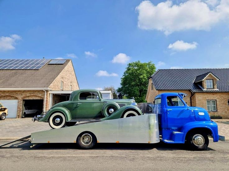 an old truck is being towed by a flatbed trailer in front of some houses