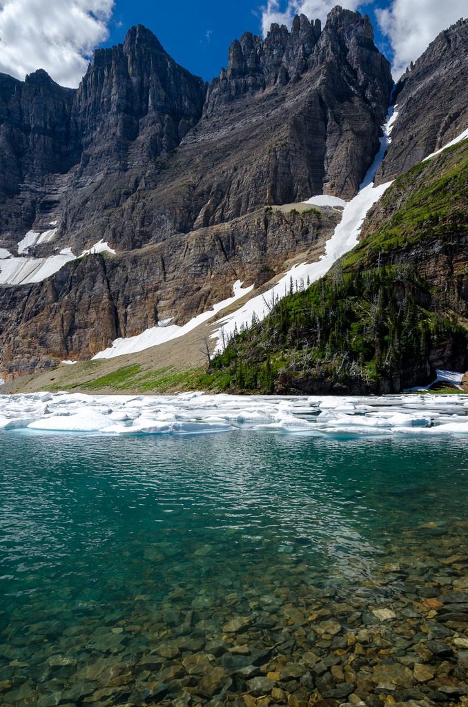 the mountains are covered in snow and green grass, while clear water is below them