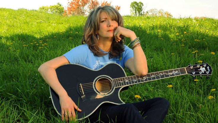 a woman sitting in the grass with an acoustic guitar