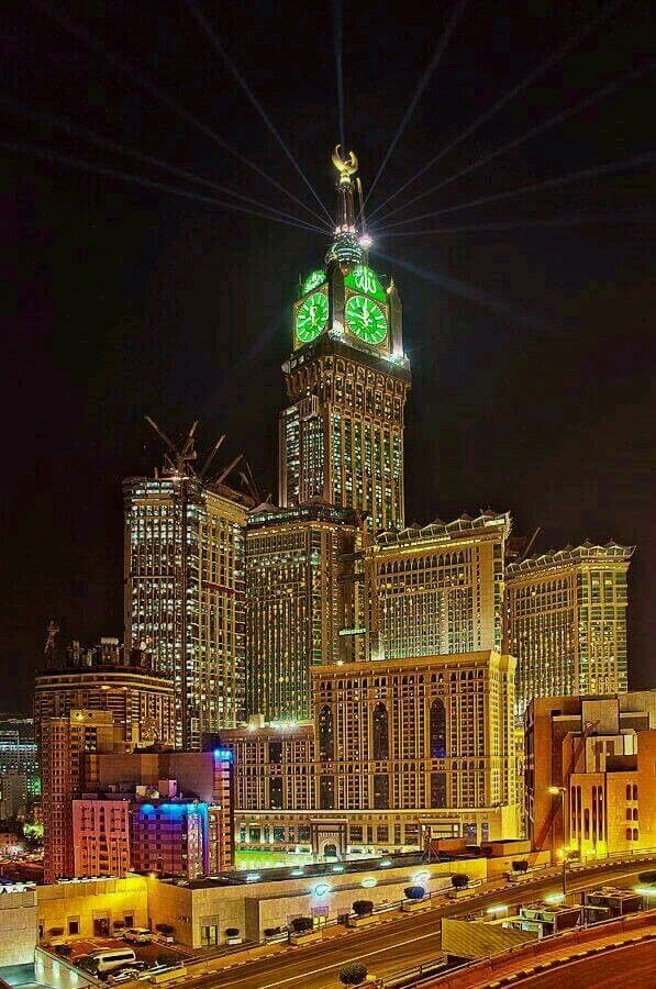 a large clock tower in the middle of a city with lights on it's sides