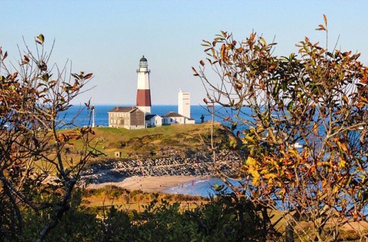 a light house sitting on top of a lush green hillside next to the ocean with trees in front of it