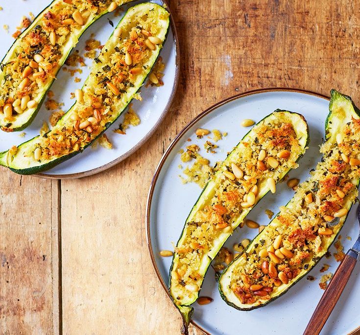 two white plates topped with stuffed zucchini on top of a wooden table next to utensils