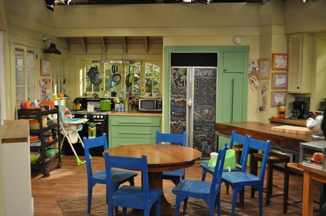 a kitchen filled with lots of wooden furniture and green doors on the windowsills