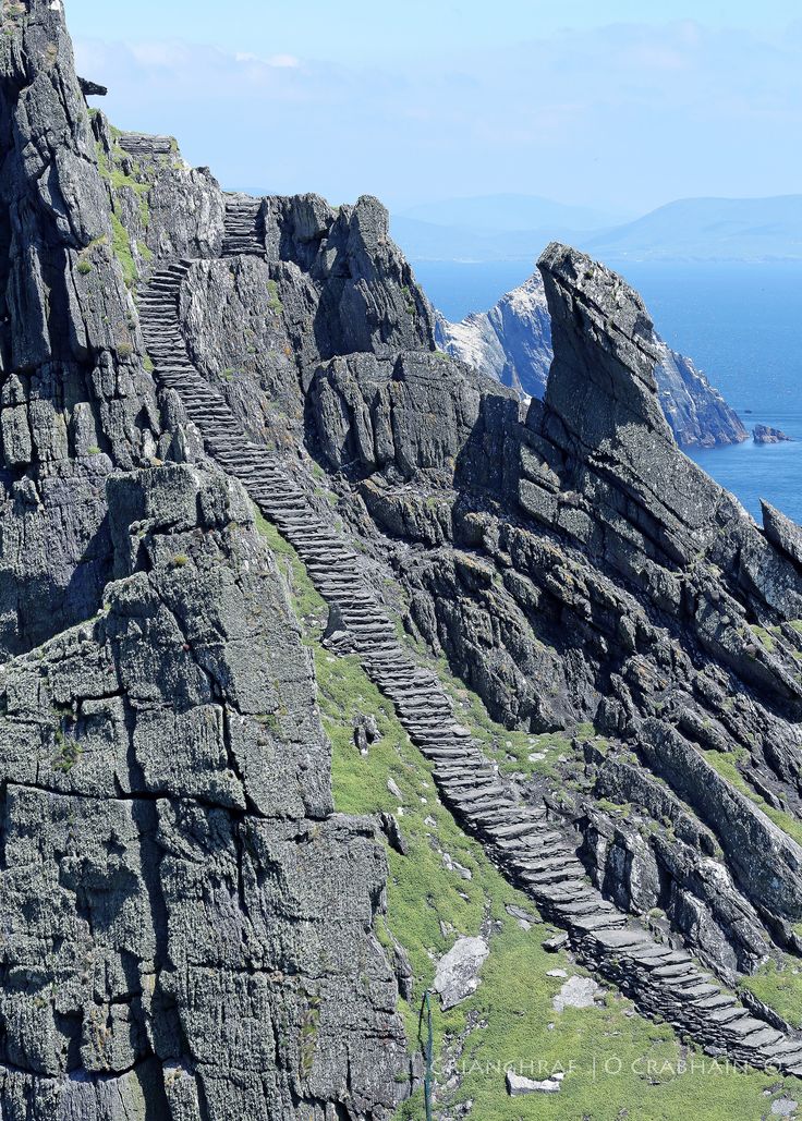 stairs leading up to the top of a rocky cliff by the ocean with mountains in the background