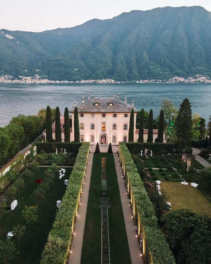 an aerial view of a large house in the middle of a lake with mountains in the background