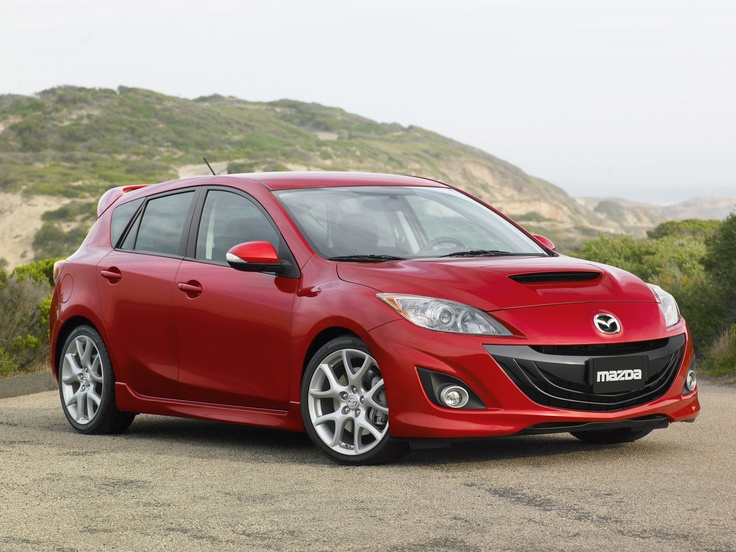 a red car parked on the side of a road near some trees and hills in the background