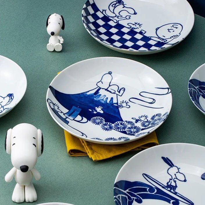 snoopy dog figurines sitting on top of blue and white plates with cartoon characters