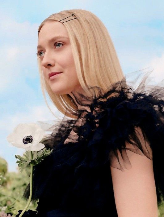 a woman with long blonde hair and a flower in her left hand, wearing a black dress