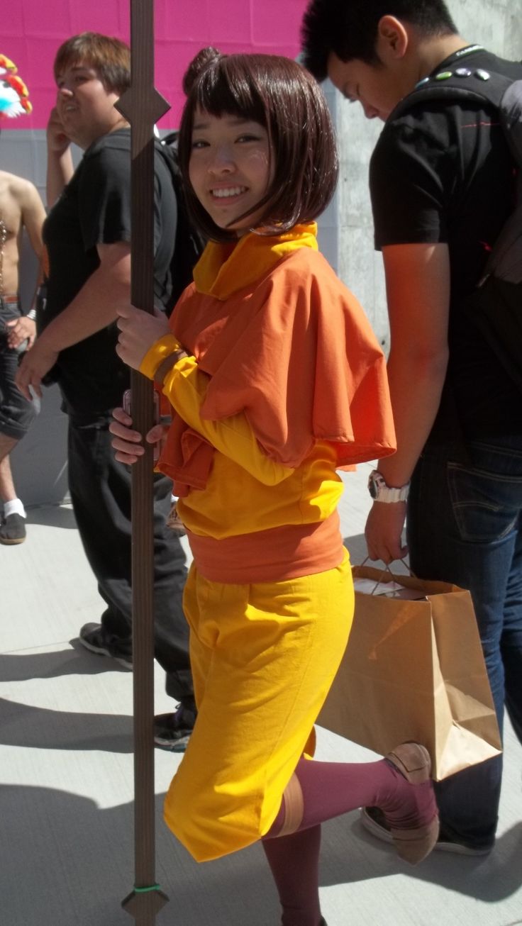 a woman in an orange outfit is holding a brown bag and smiling at the camera