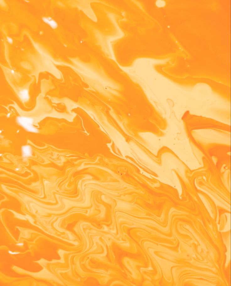 an orange and yellow liquid swirls in the air with water droplets on it's surface