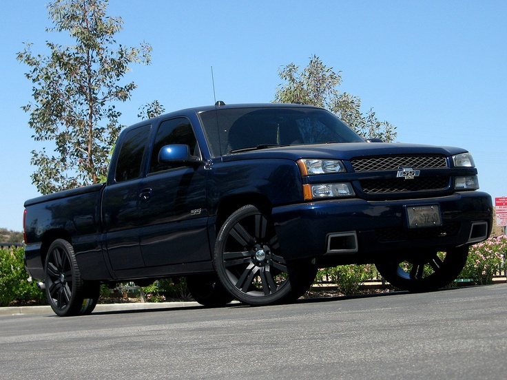 a black truck is parked on the side of the road in front of some bushes