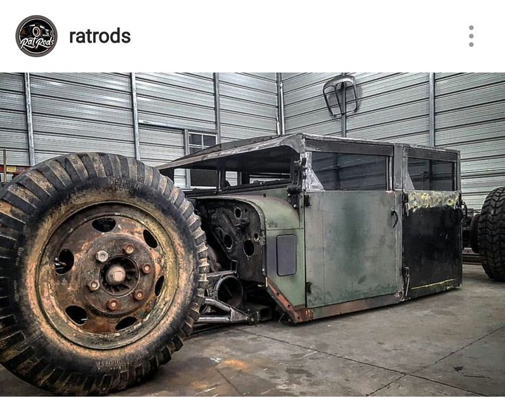 an old truck is parked in front of a building with large tires on it's sides