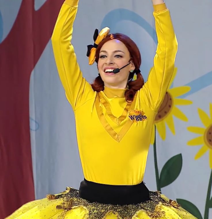 a woman in a yellow shirt and black skirt holding her arms up with both hands