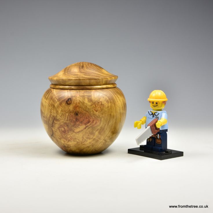 a toy soldier next to a wooden urn on a white surface with a gray background