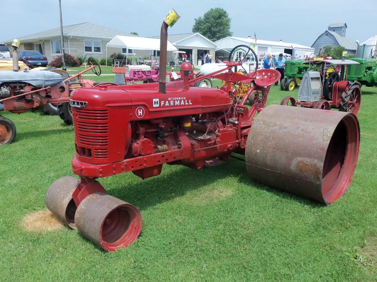 an old red farmall tractor sitting on top of grass next to other antique tractors