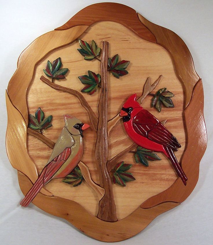 two red birds sitting on top of a wooden plate with leaves and branches around it