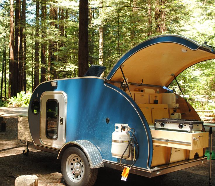 a camper trailer parked in the woods with its door open and it's hood up