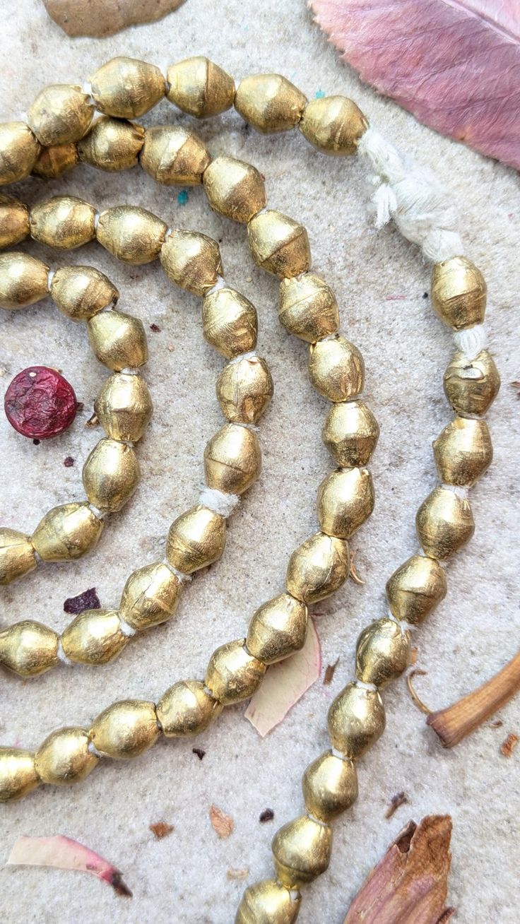 a long gold bead necklace laying on top of a white carpet next to a leaf