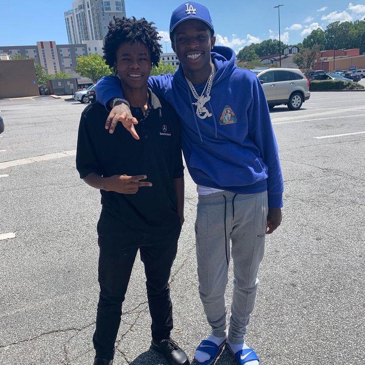 two young men standing next to each other in a parking lot with buildings in the background