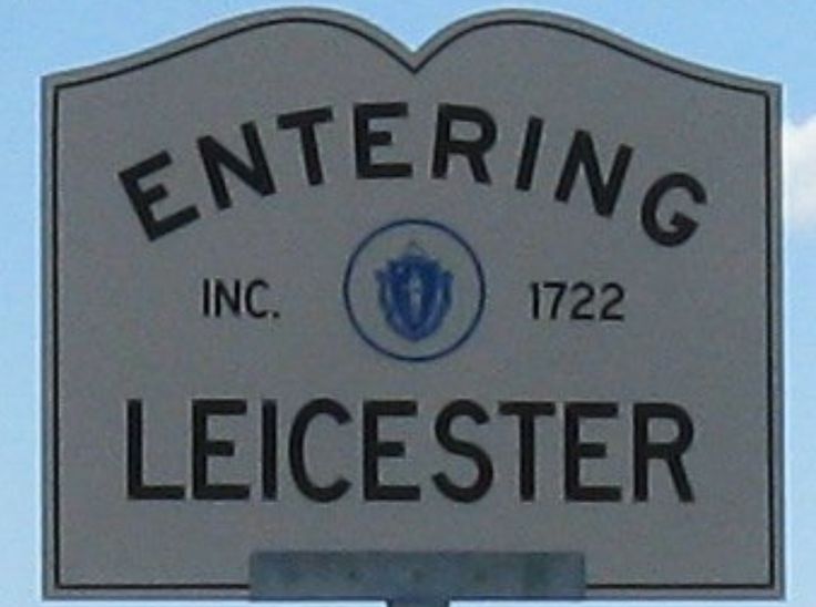 a white sign that reads entering to the town of leigester in front of a blue sky