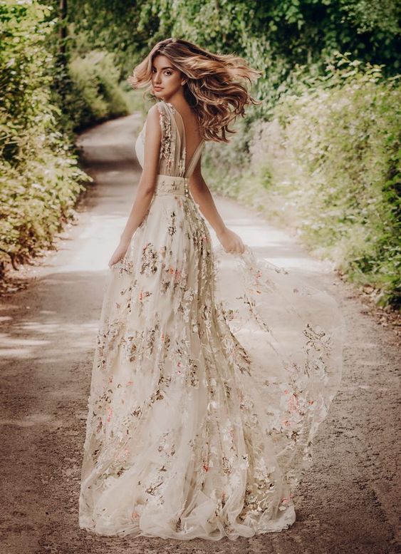 a woman in a long dress walking down a dirt road with her hair blowing in the wind