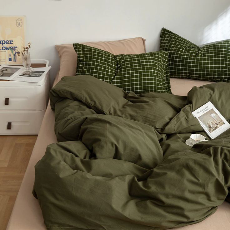 an unmade bed with green sheets and pillows on it, next to a white nightstand