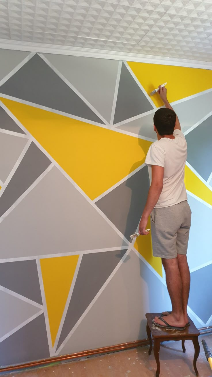 a man painting a wall with yellow and grey triangles