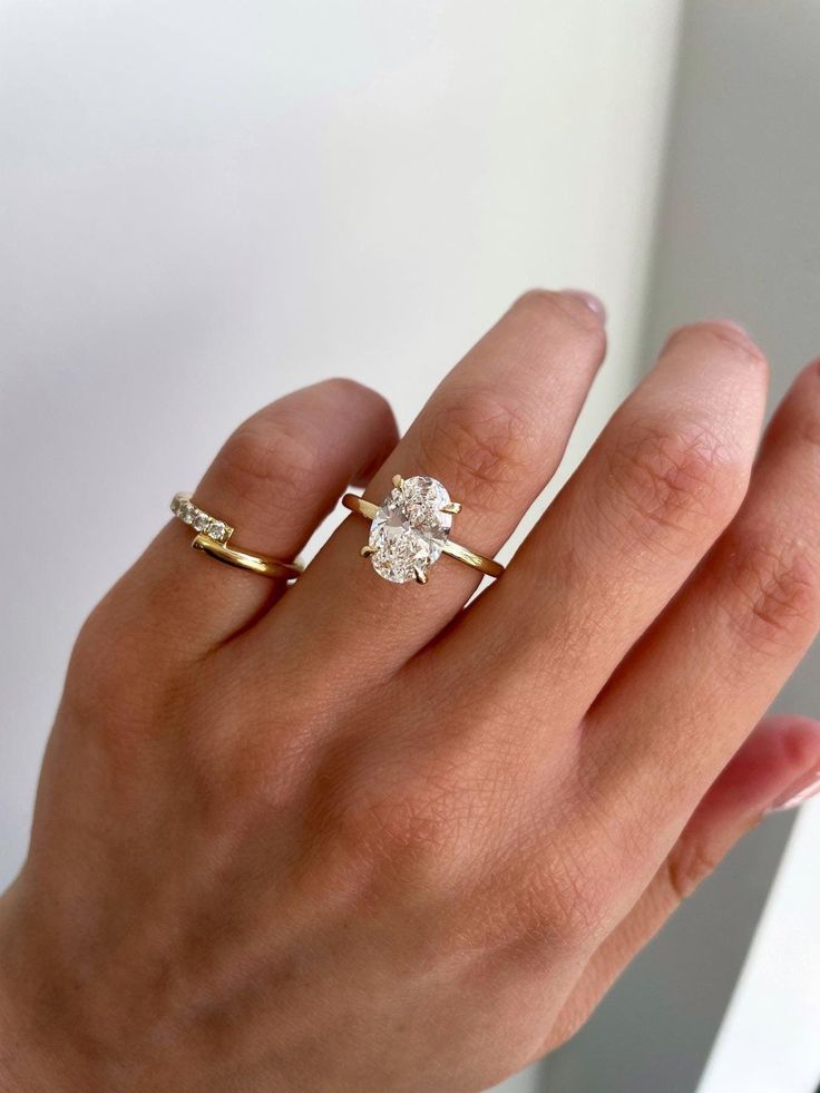 a woman's hand with two gold rings on top of her finger and the ring has an oval shaped diamond