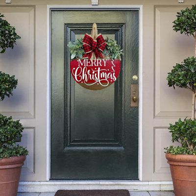 a merry christmas door hanger on the side of a house with potted plants