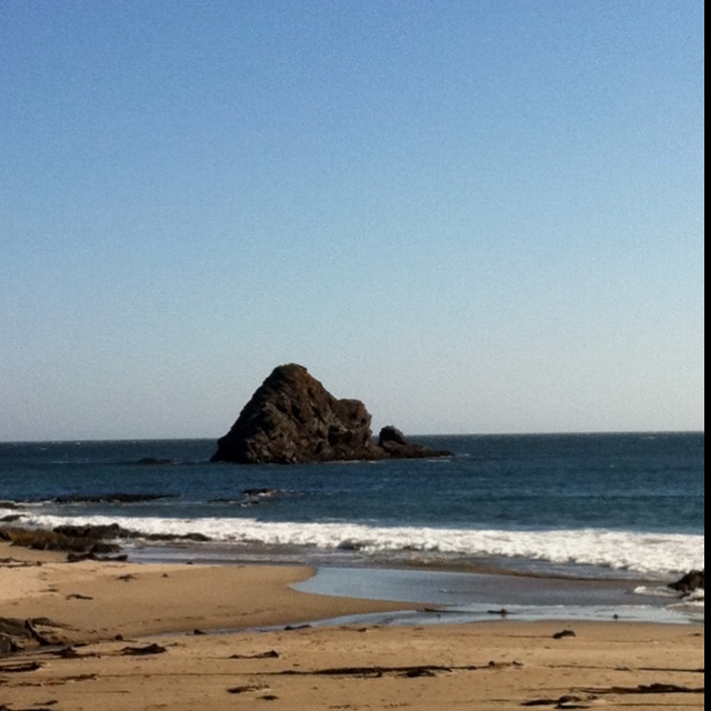 a person walking on the beach with a surfboard under their arm and an island in the background