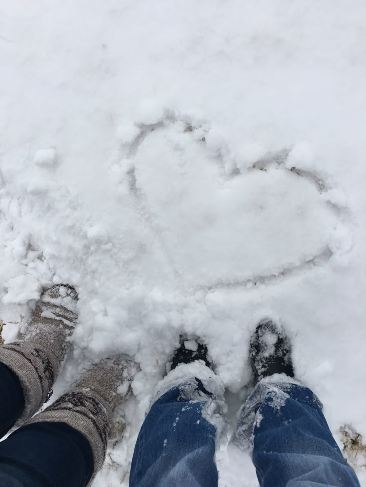 two people are standing in the snow with their feet up and heart drawn in the snow