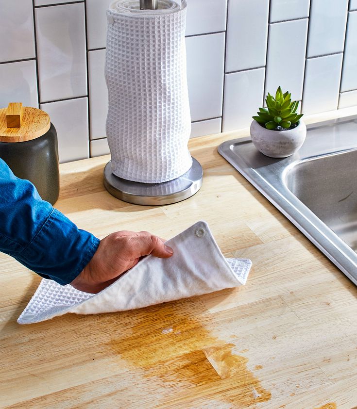 a person wiping up some paper on a kitchen counter top with a cloth over it