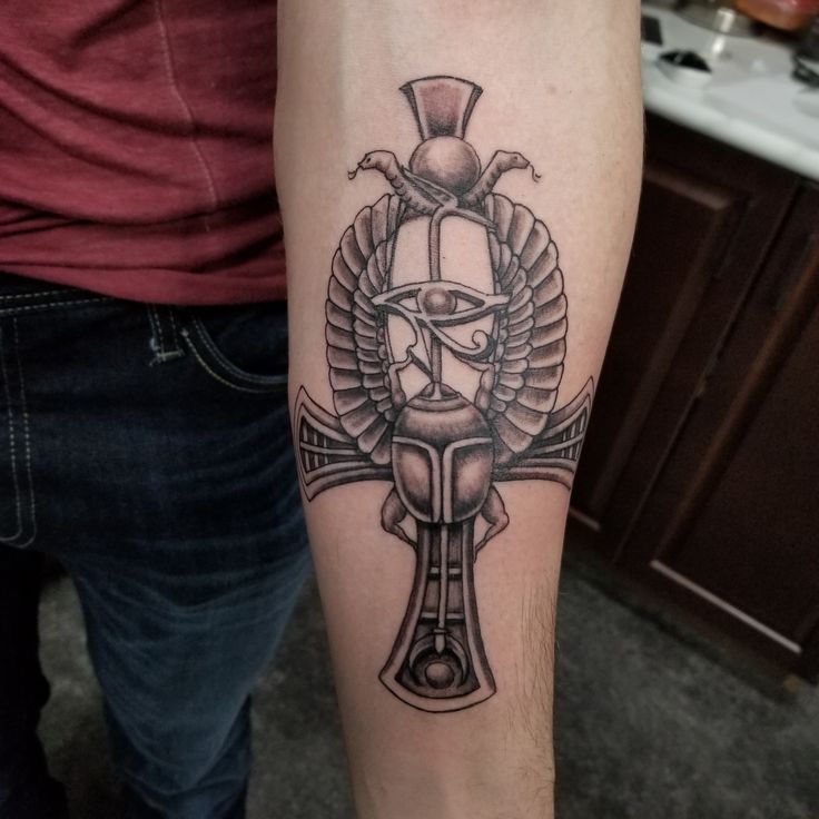 a man's arm with a cross and an egyptian god tattoo on the forearm