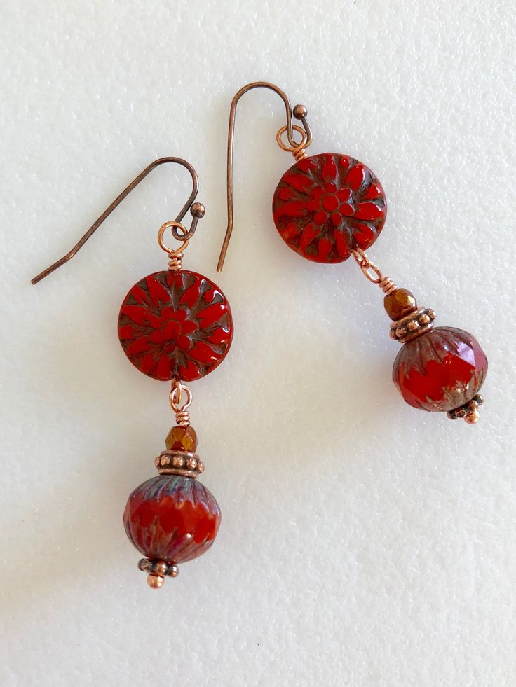 two red beads are hanging from earrings on a white surface