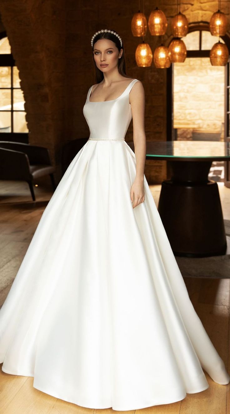 a woman in a white wedding dress standing on a wooden floor next to a chandelier