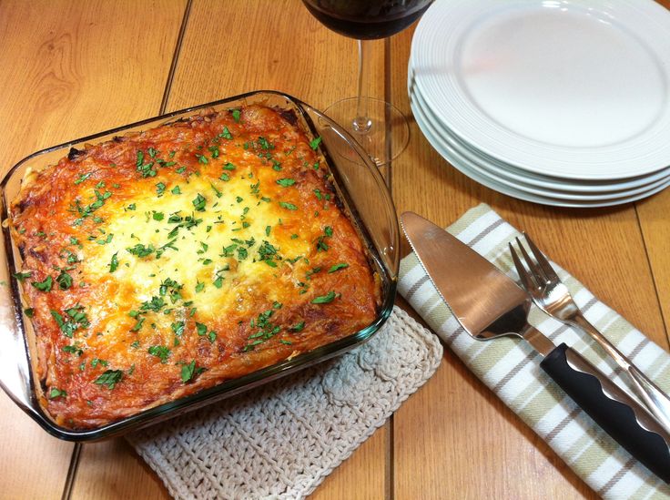 a casserole dish on a place mat next to silverware and wine glasses