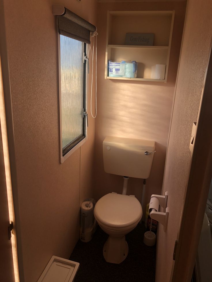 a small bathroom with a toilet, sink and window in the corner on the wall