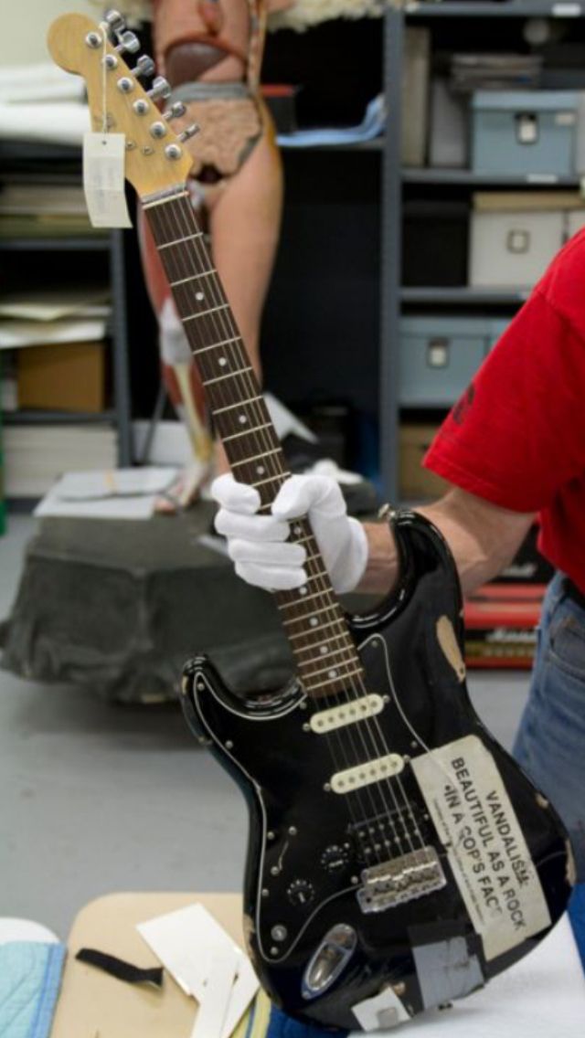 a man in a red shirt is holding a black guitar and another person wearing a cowboy hat