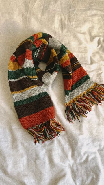 a multicolored scarf laying on top of a white bed sheet with an orange, green, yellow and red stripe