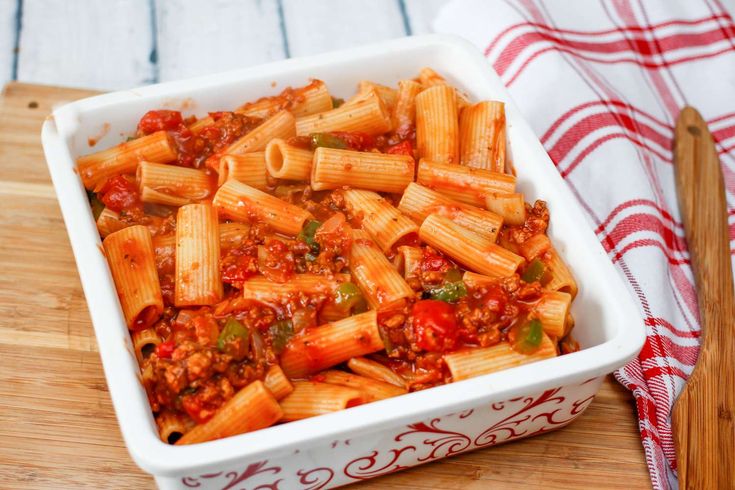 a casserole dish filled with pasta and sauce on a wooden cutting board next to a red and white towel